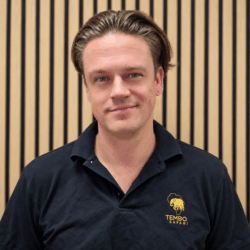 Smiling man in a black polo shirt with Tembo Safari logo, posed in front of a wooden slat wall.